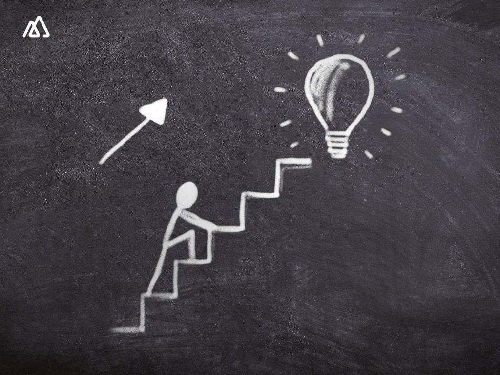 man climbing on a ladder to reach a lightbulb drawing on chalkboard